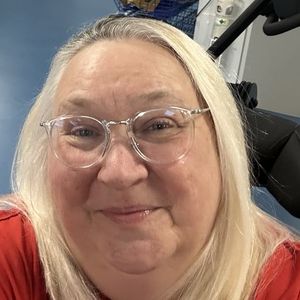 Angela, a blonde woman in her late 50s, smiles at the camera. She is in the gym at the hospital where she is being rehabilitated following a spinal injury.