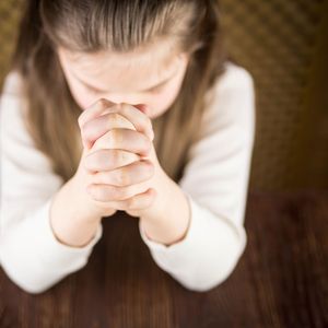 headshot of a girl praying with closed hands in front of her face