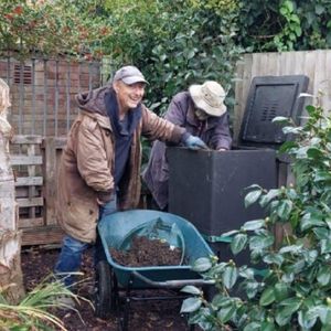 two male volunteers smiling while moving compost with a wheelbarrow in community garden