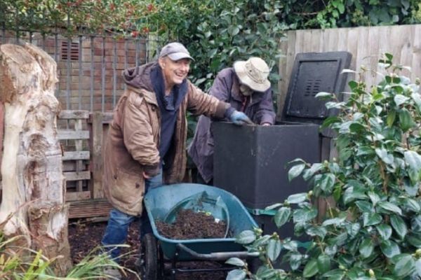 two male volunteers smiling while moving compost with a wheelbarrow in community garden